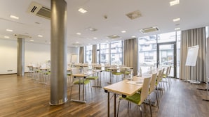 A spacious conference room with multiple tables and chairs, large windows, and a whiteboard.