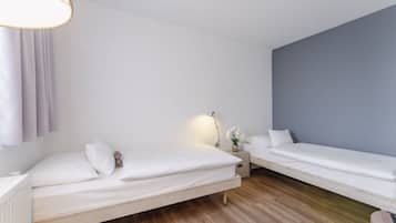 A modern hotel room with two single beds, a nightstand with a lamp, and a window with curtains.