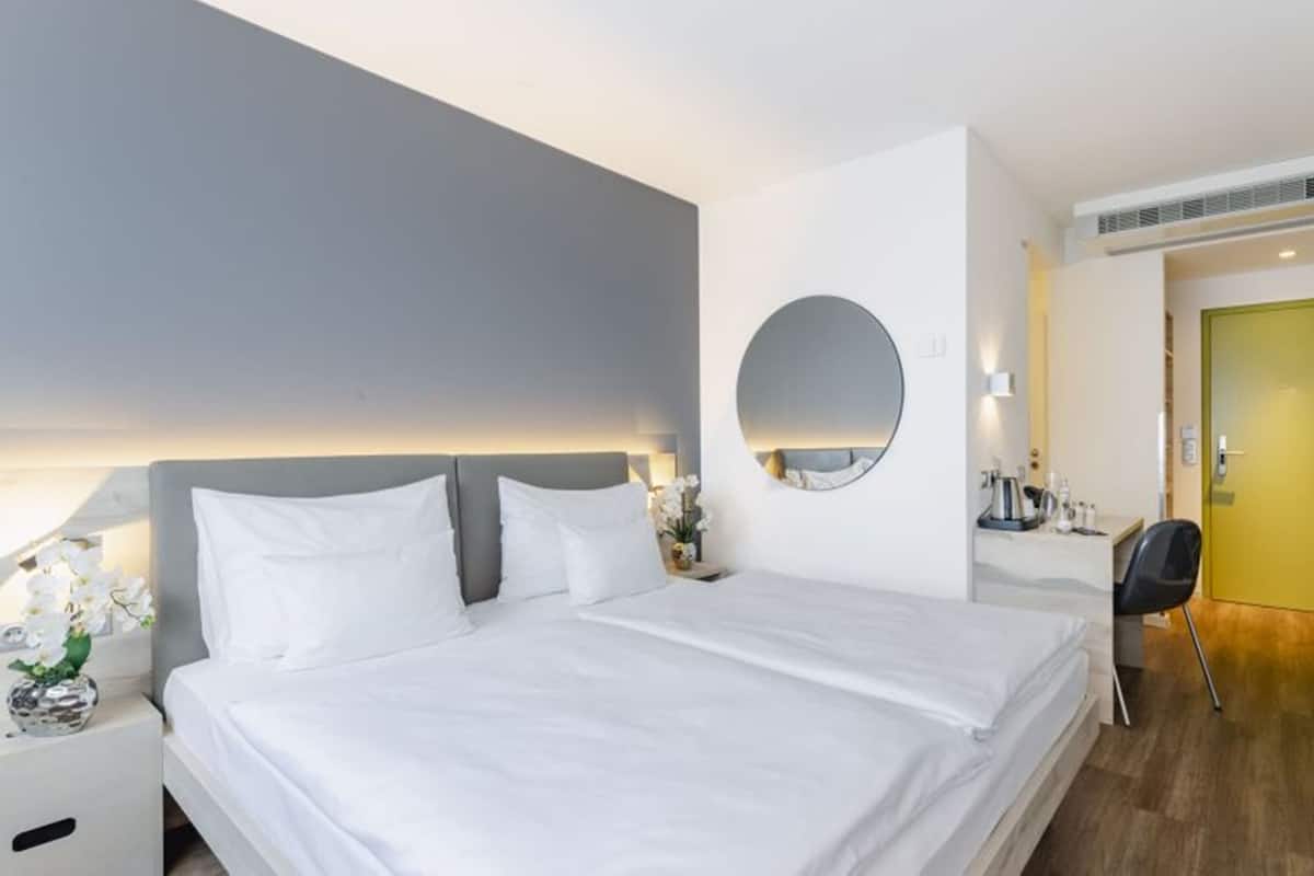 A modern hotel room with a large bed, bedside table, and a mirror.