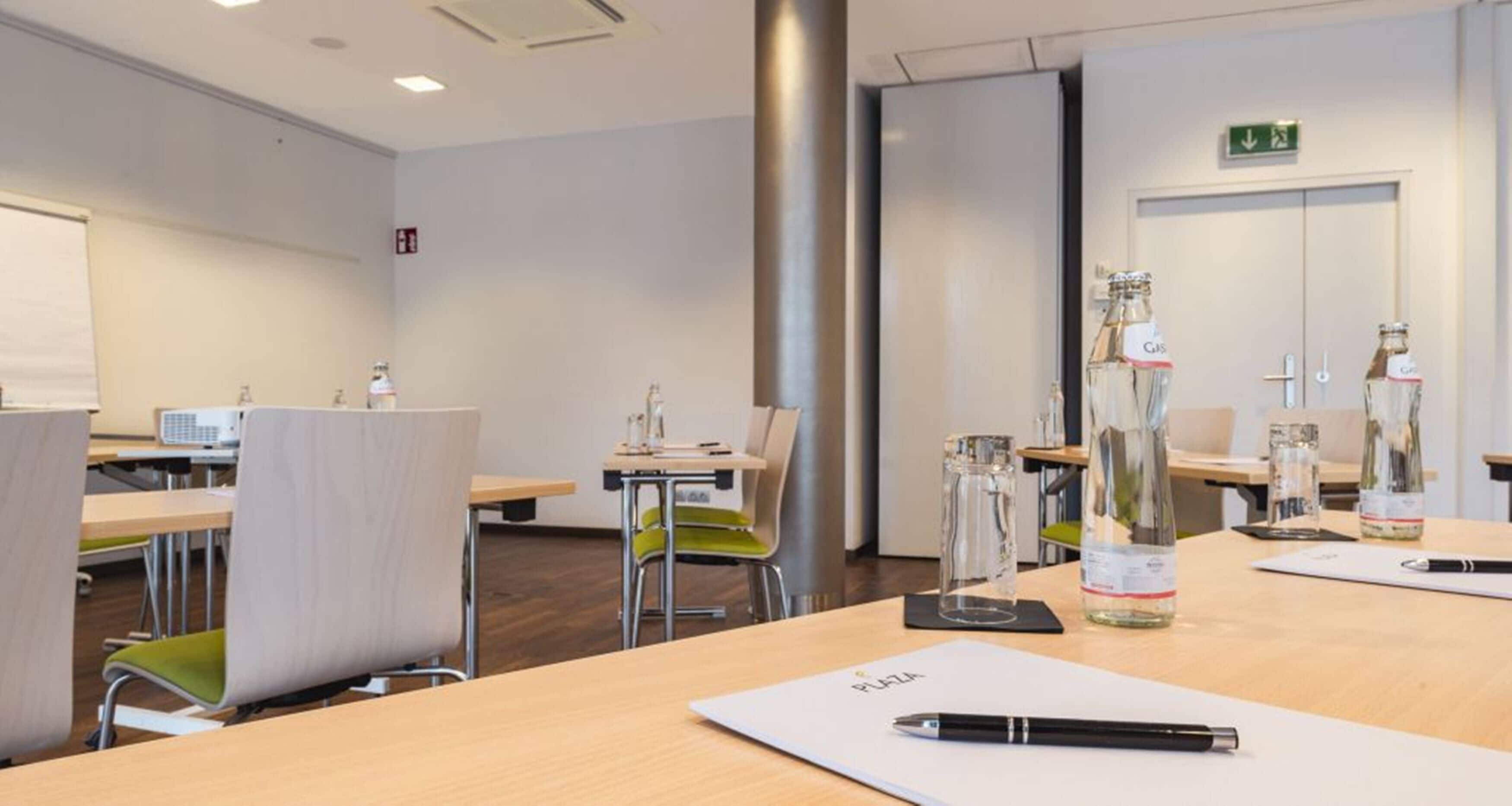 Ein Konferenzraum mit Holztischen, Stühlen und einer Whiteboard-Tafel.