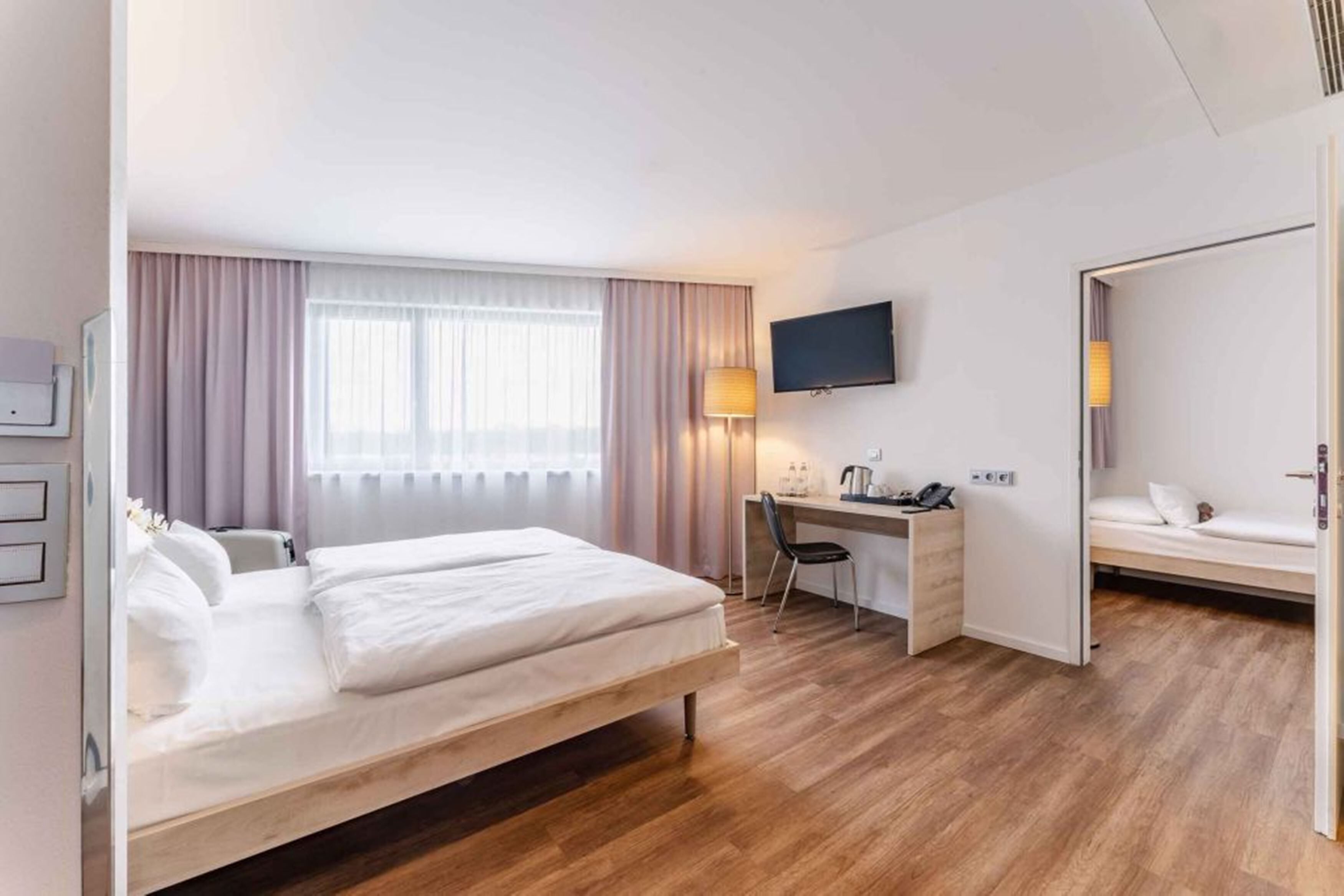Habitación de hotel con cama, escritorio, silla, televisor y una pequeña zona de estar.