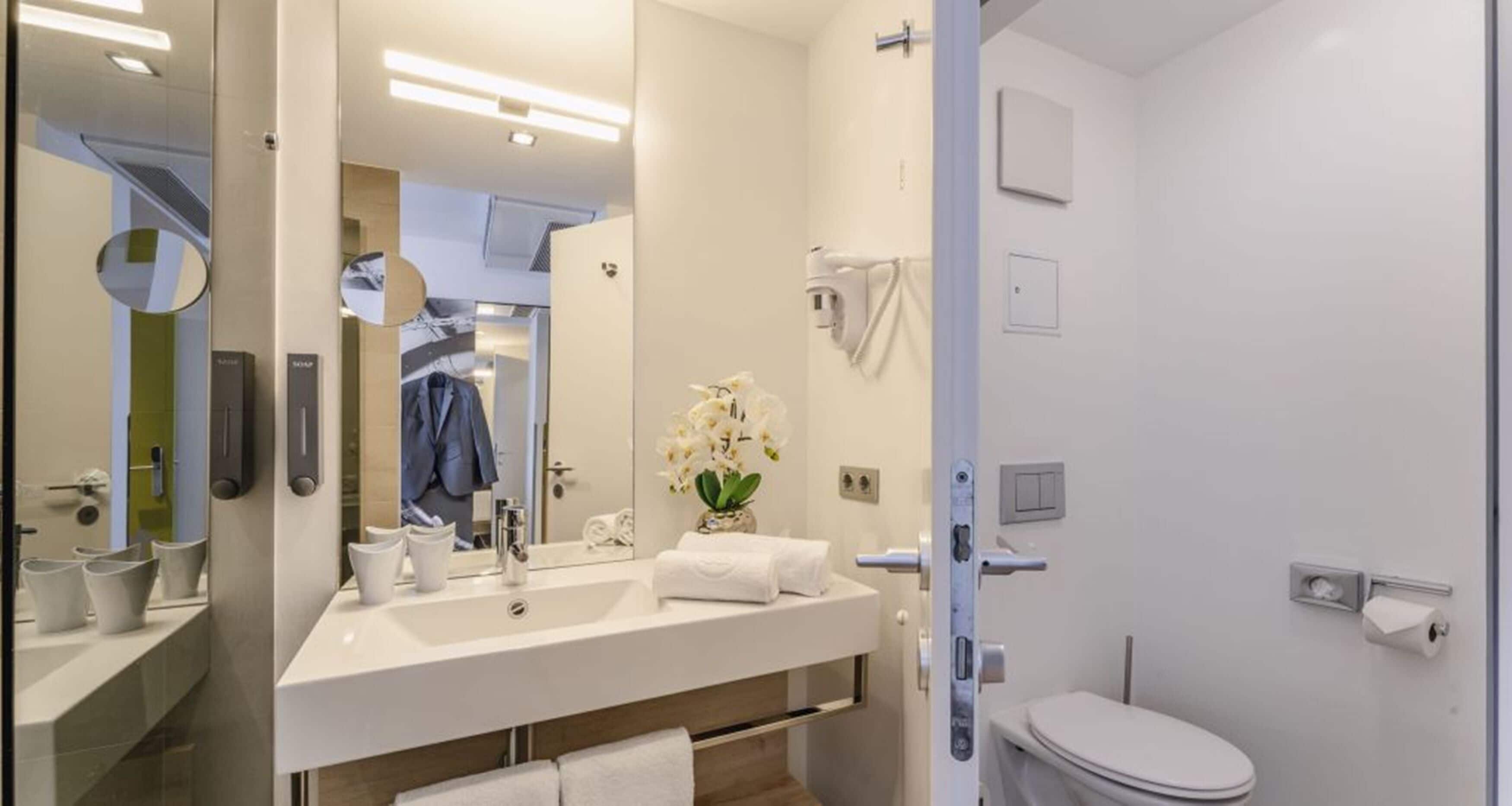 Un baño moderno con un espejo grande, un lavabo y un inodoro.