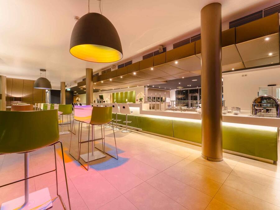 Un restaurante moderno con sillas altas, una barra y lámparas colgantes.