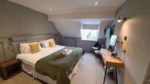 A bedroom with a bed, a desk, a chair, a window, and a television. - The Priory Inn (Tetbury)