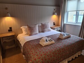 A neatly made bed with floral bedding, two bedside lamps, and a window with curtains.