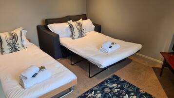 A hotel room with two single beds, each with a white mattress and matching pillows, a dark headboard, and a blue patterned rug on the floor.