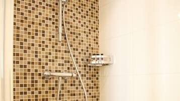 A shower area with a tiled wall, a handheld showerhead, and a wall-mounted control panel.