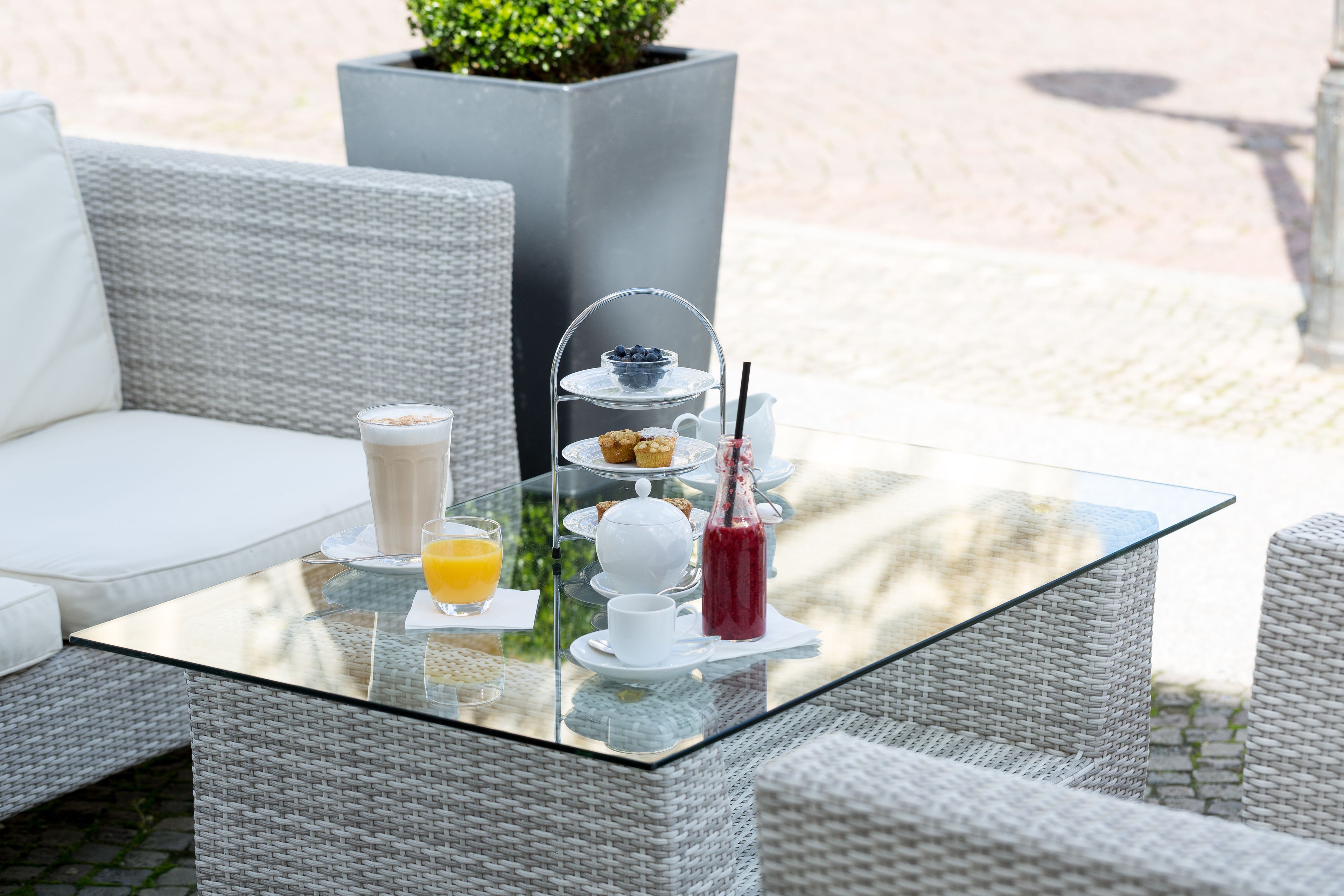 A glass-top table with a tiered tea service, white cups, and a glass of orange juice.