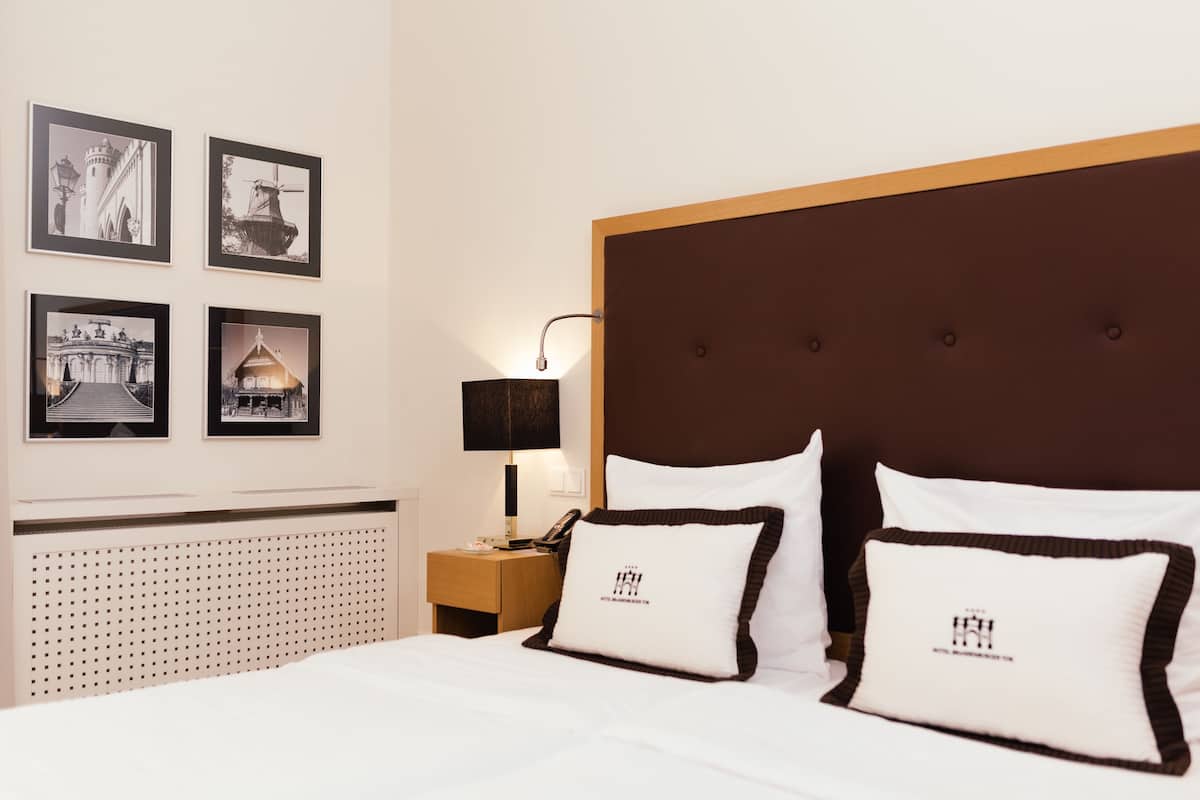 Quarto de hotel com uma cama grande, cabeceira de madeira e quatro quadros na parede.