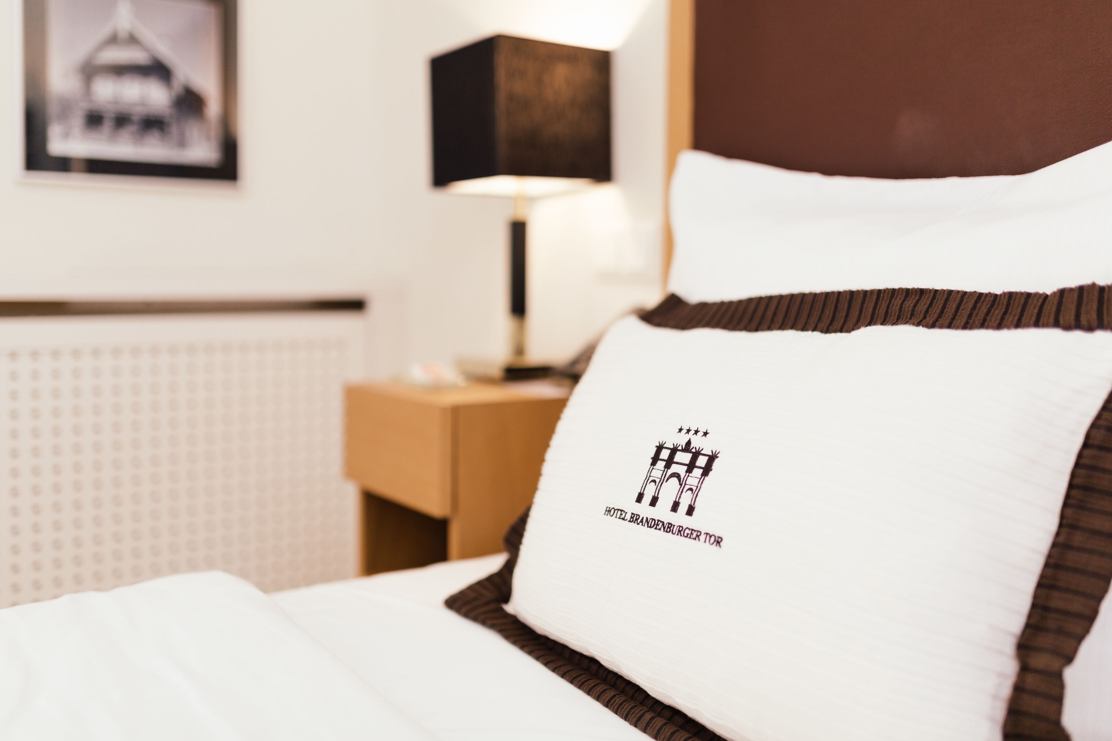 A hotel room with a neatly made bed, a lamp on a bedside table, and a framed picture on the wall.