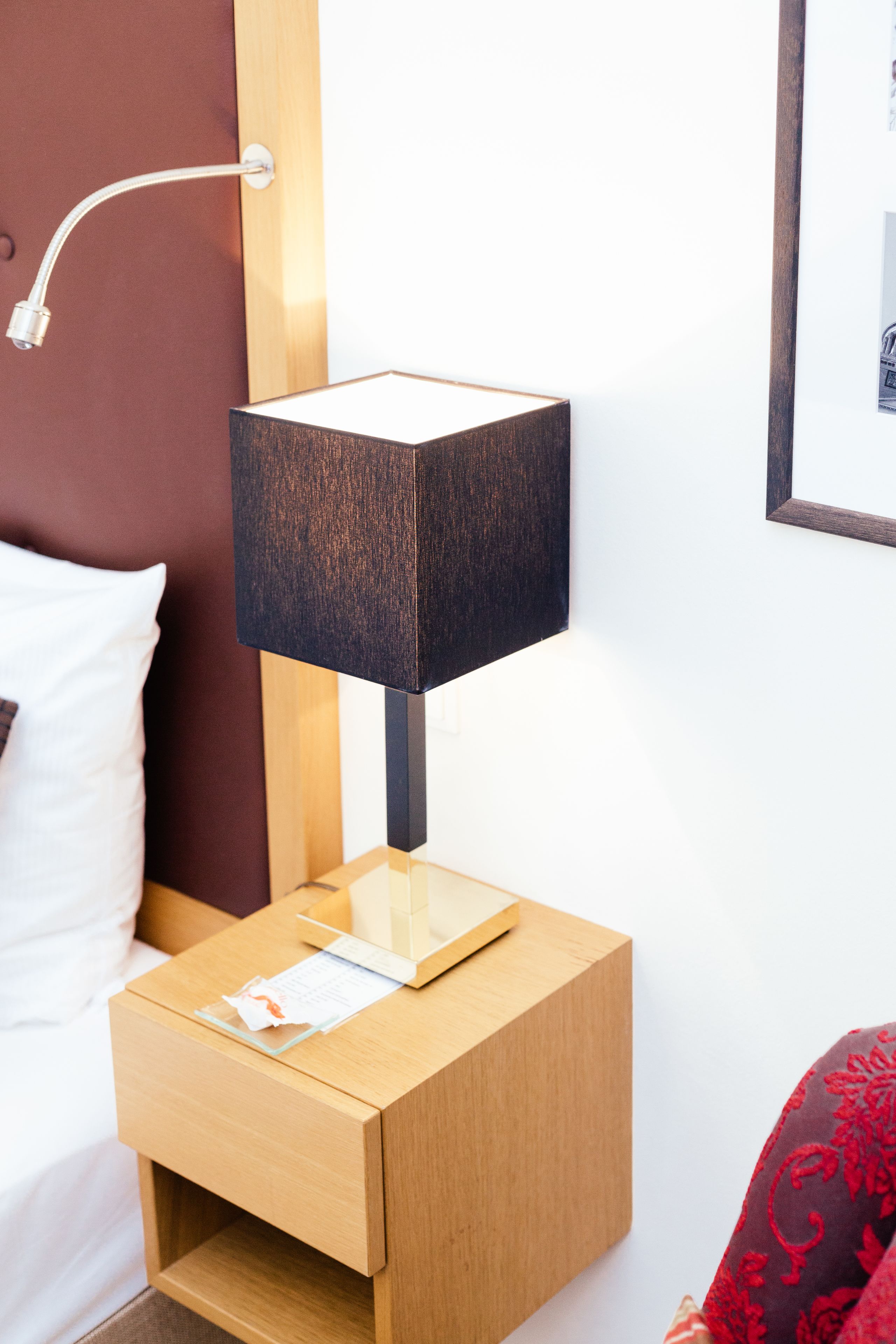 Uma mesa de cabeceira de madeira com uma luminária preta, um travesseiro branco e um quadro na parede.