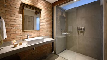 Un baño moderno con pared de ladrillo, un espejo grande, un lavamanos y una ducha con cerramiento de vidrio.