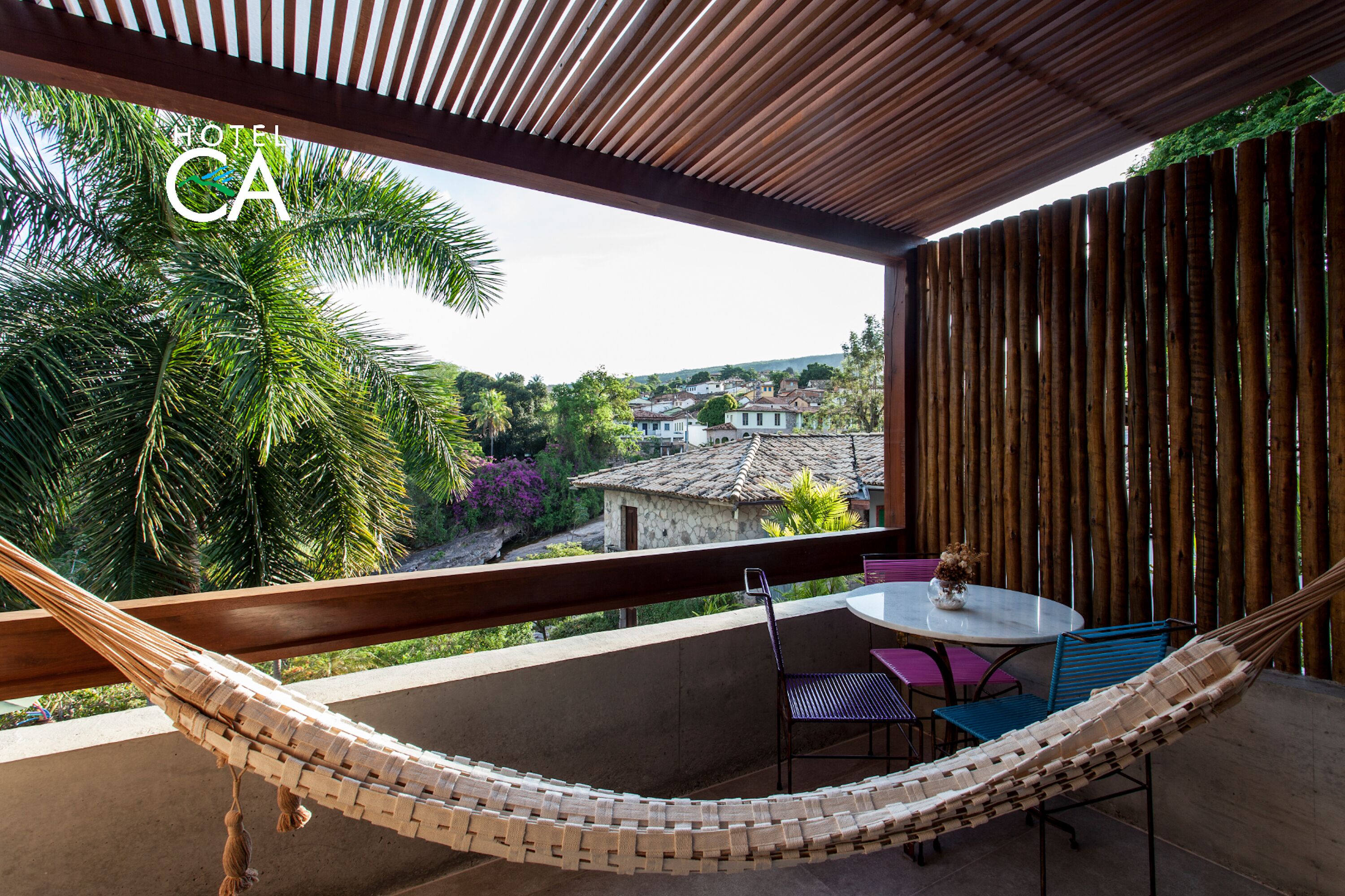 A hammock on a balcony with a view of a town and palm trees.
