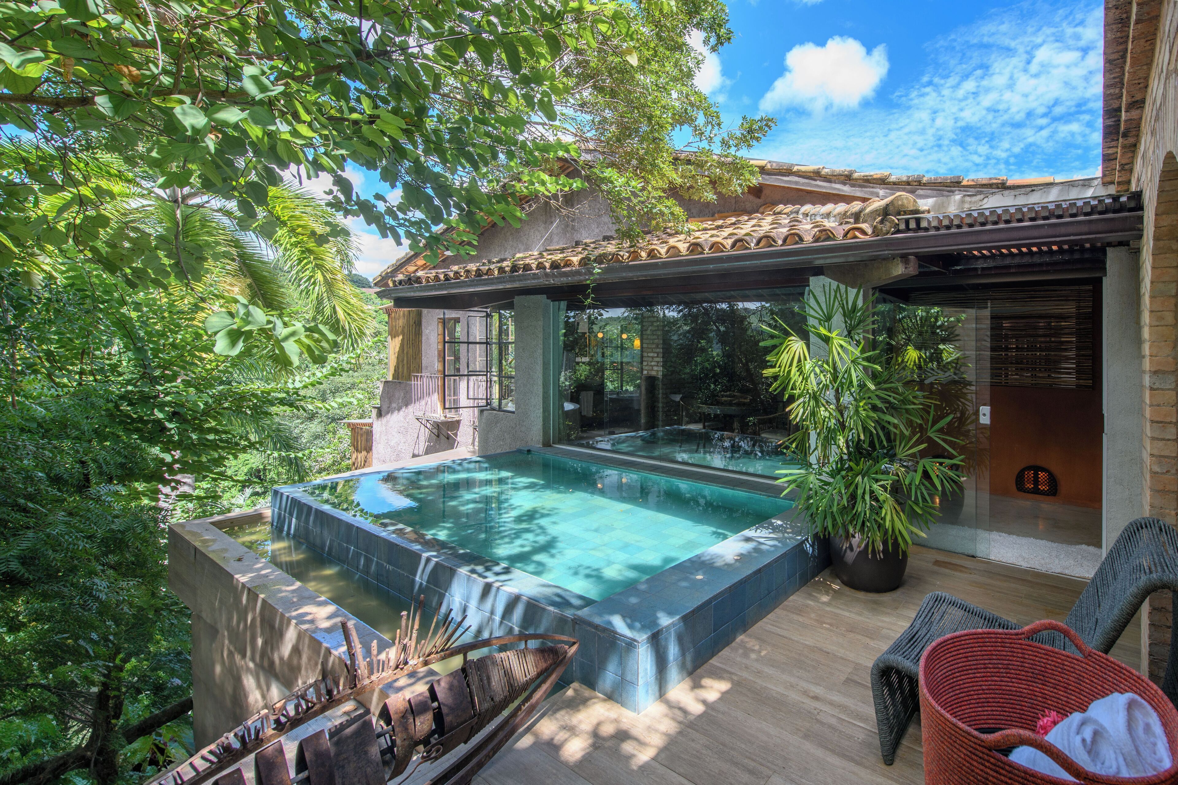 Uma piscina infinita no terraço com vista para o céu, rodeada por vegetação exuberante e um telhado tradicional em azulejos.