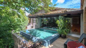 Uma piscina infinita no terraço com vista para o céu, rodeada por vegetação exuberante e um telhado tradicional em azulejos.