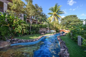 A swimming pool with a stone border, surrounded by lush greenery and palm trees. - Hotel Canto das Águas (Lençóis)