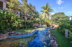 Piscina com borda de pedra, rodeada por vegetação exuberante e palmeiras.