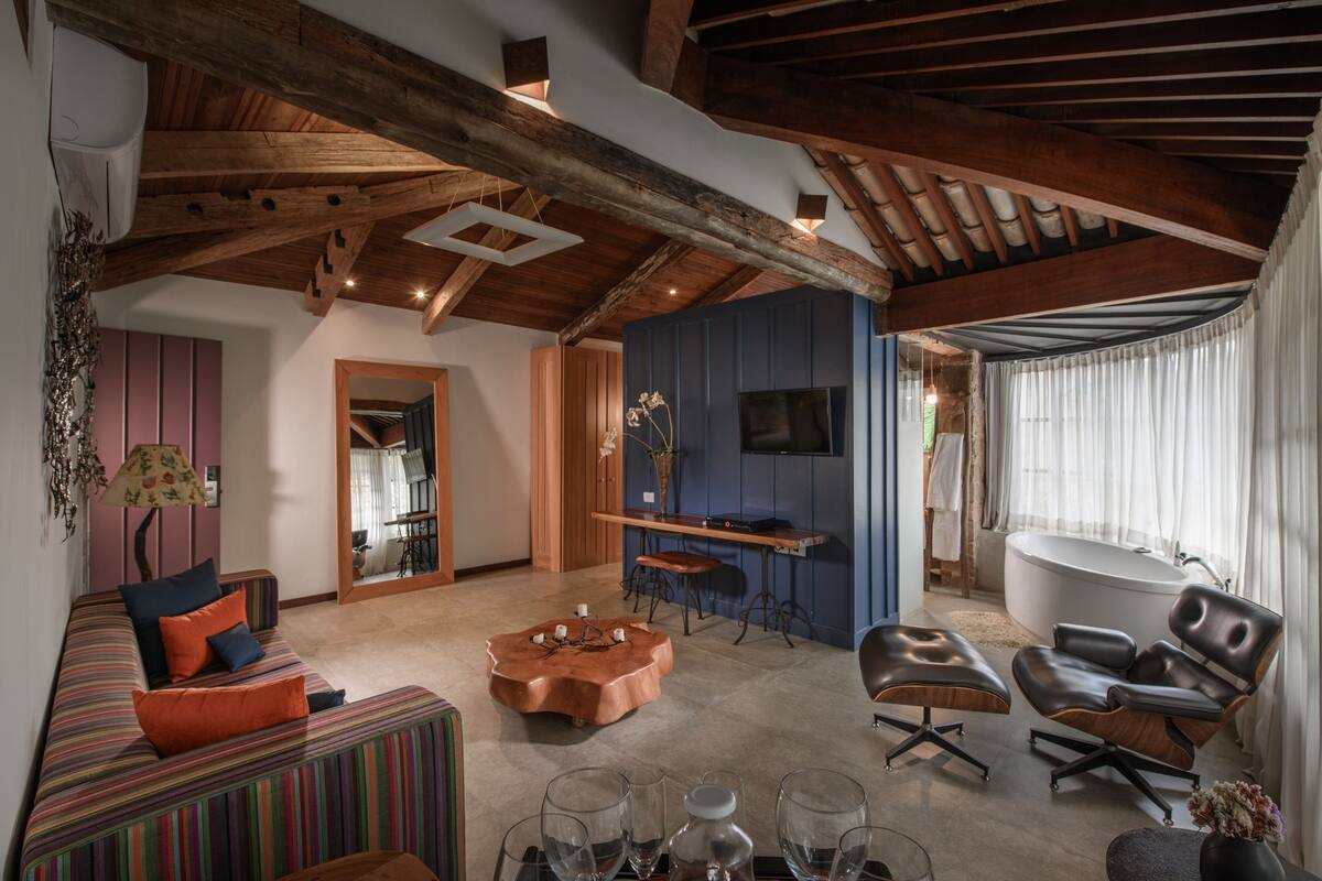 A spacious living area with a wooden ceiling, a large sofa, a coffee table, and a seating area with a chair.