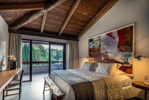 Un dormitorio con una cama grande, vigas de madera en el techo, un comedor con mesa y sillas, y un ventanal con vistas a zonas verdes.