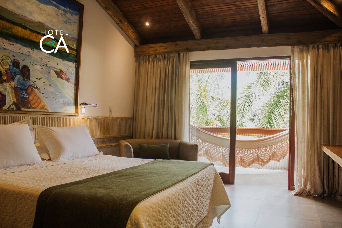 A hotel room with a bed, a hammock, and a view of palm trees.
