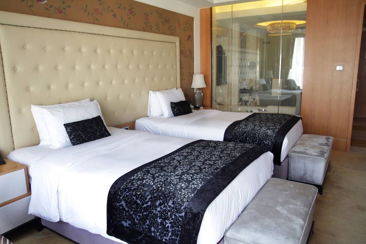 A hotel room with two beds, a large tufted headboard, a mirror, and a wooden door.