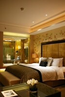 A hotel room with a large bed, a bedside table with a vase of flowers, a mirror, and a wall with floral wallpaper.