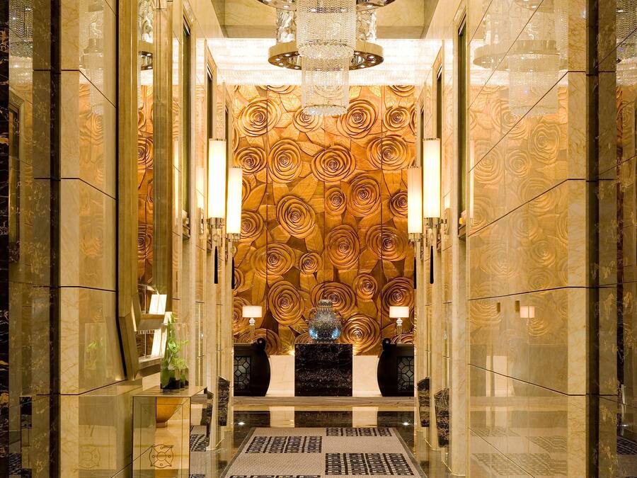 A luxurious hallway with a marble floor, a central chandelier, and a floral patterned wall.
