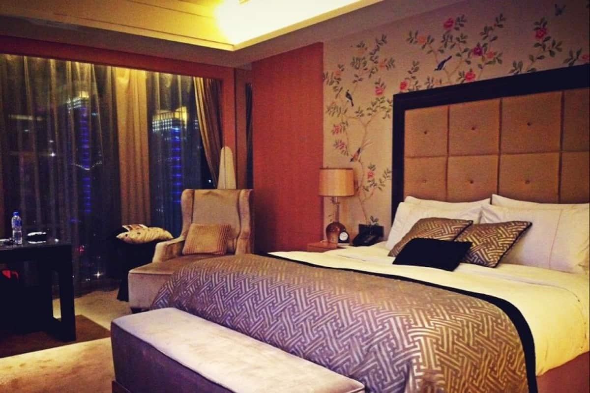 A hotel room with a large bed, a chair, a desk, and a window with curtains.