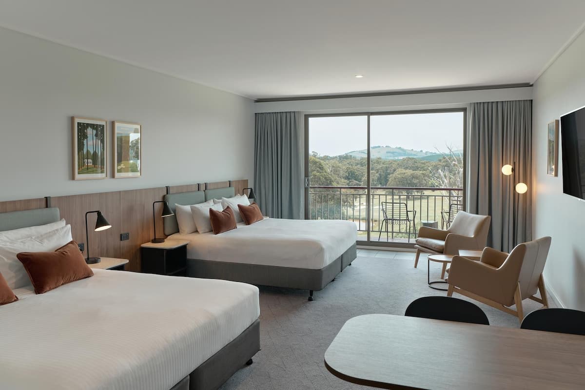A hotel room with two beds, a balcony with a view, and a seating area.
