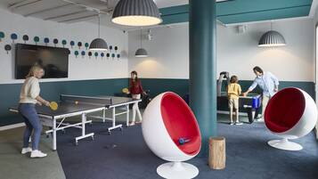 A ping pong table, a large TV, and a group of people playing ping pong in a room with modern furniture and a teal accent wall.