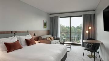A modern hotel room with a large bed, a sofa, a small table, and a balcony with a view.