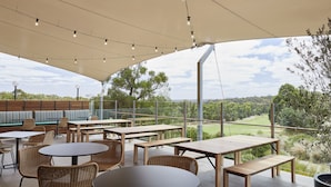 An outdoor patio area with wooden tables and chairs, a seating area with cushions, and a view of the landscape. - RACV Goldfields Resort (Creswick)