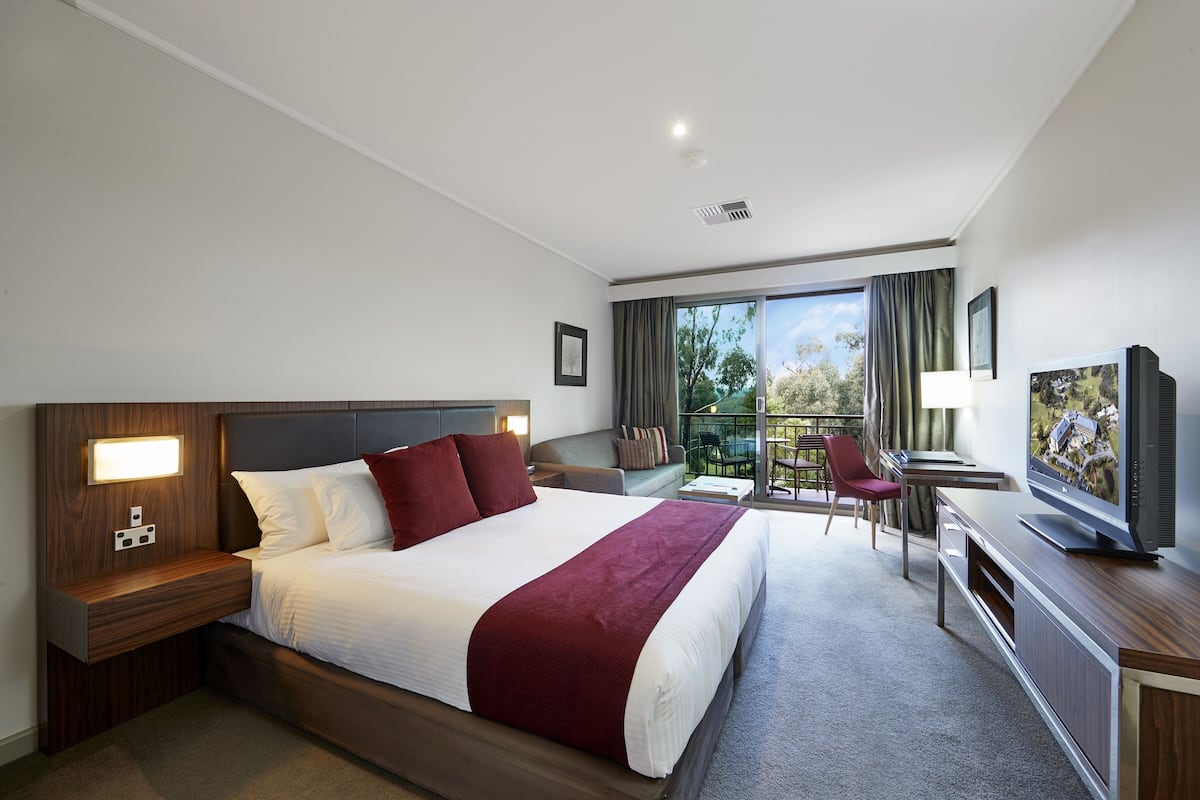 A hotel room with a large bed, a desk, a chair, a television, and a balcony with a view.