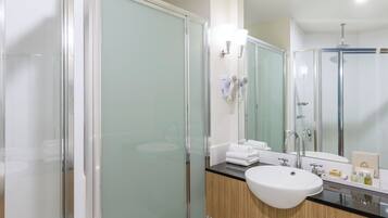 A modern bathroom with a glass shower enclosure, a sink with a wooden vanity, and a mirror with a hairdryer mounted on it.