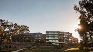 A modern building with multiple floors and large windows, surrounded by a well-maintained grassy area and trees. - RACV Goldfields Resort (Creswick)