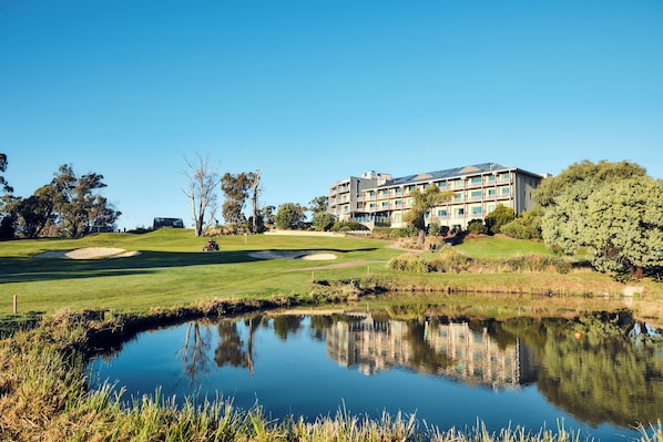 A golf course with a pond, a building with multiple floors, and surrounding greenery.