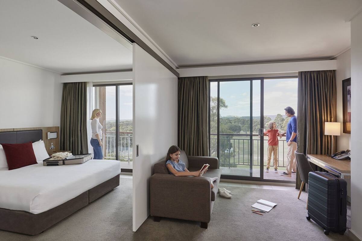 A hotel room with a bed, a sofa, a desk, and a balcony with a view.