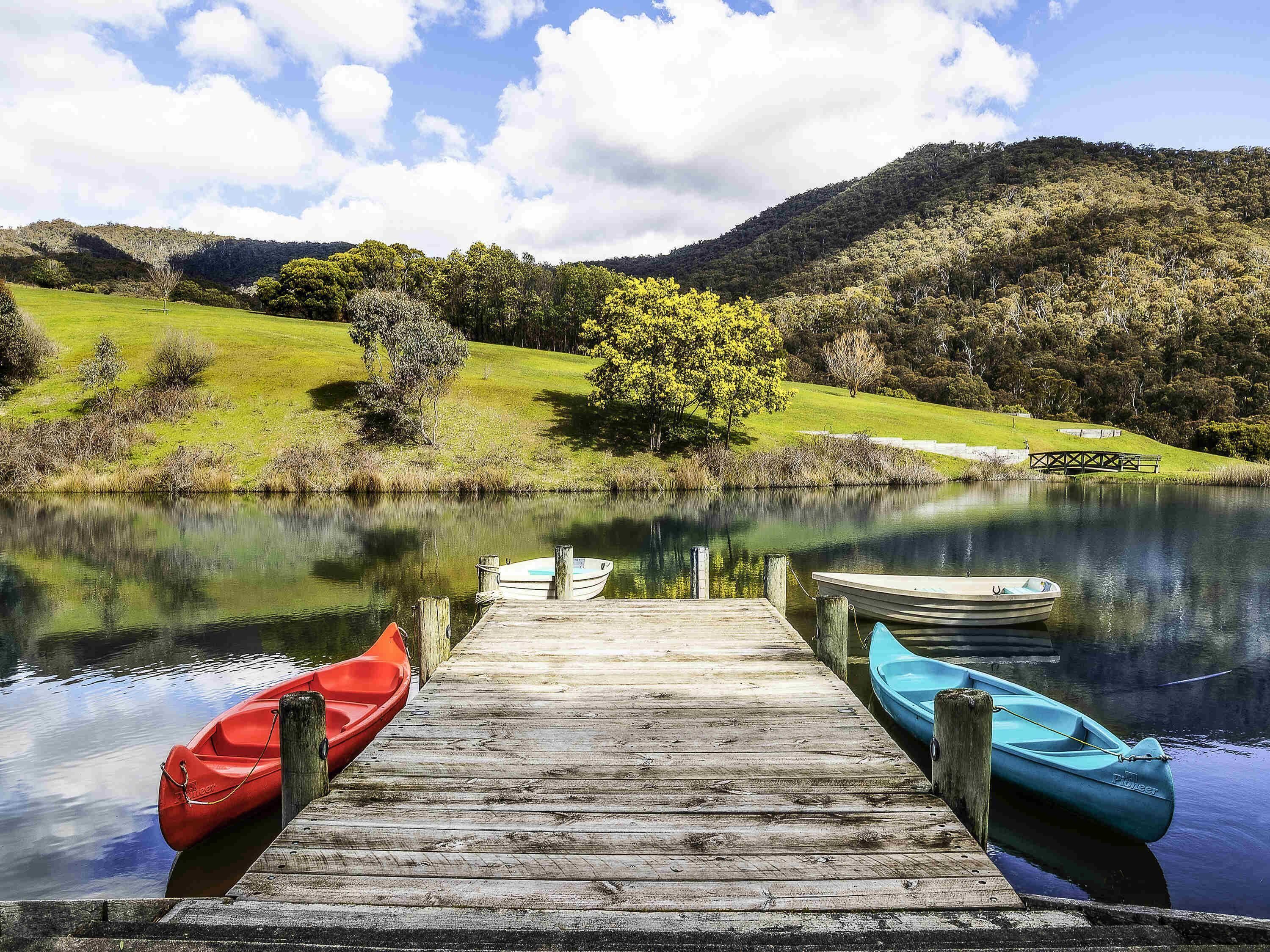 Une jetée en bois avec deux bateaux amarrés à son extrémité, un lac paisible et un paysage vallonné en arrière-plan.