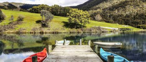 Une jetée en bois avec deux bateaux amarrés à son extrémité, un lac paisible et un paysage vallonné en arrière-plan.