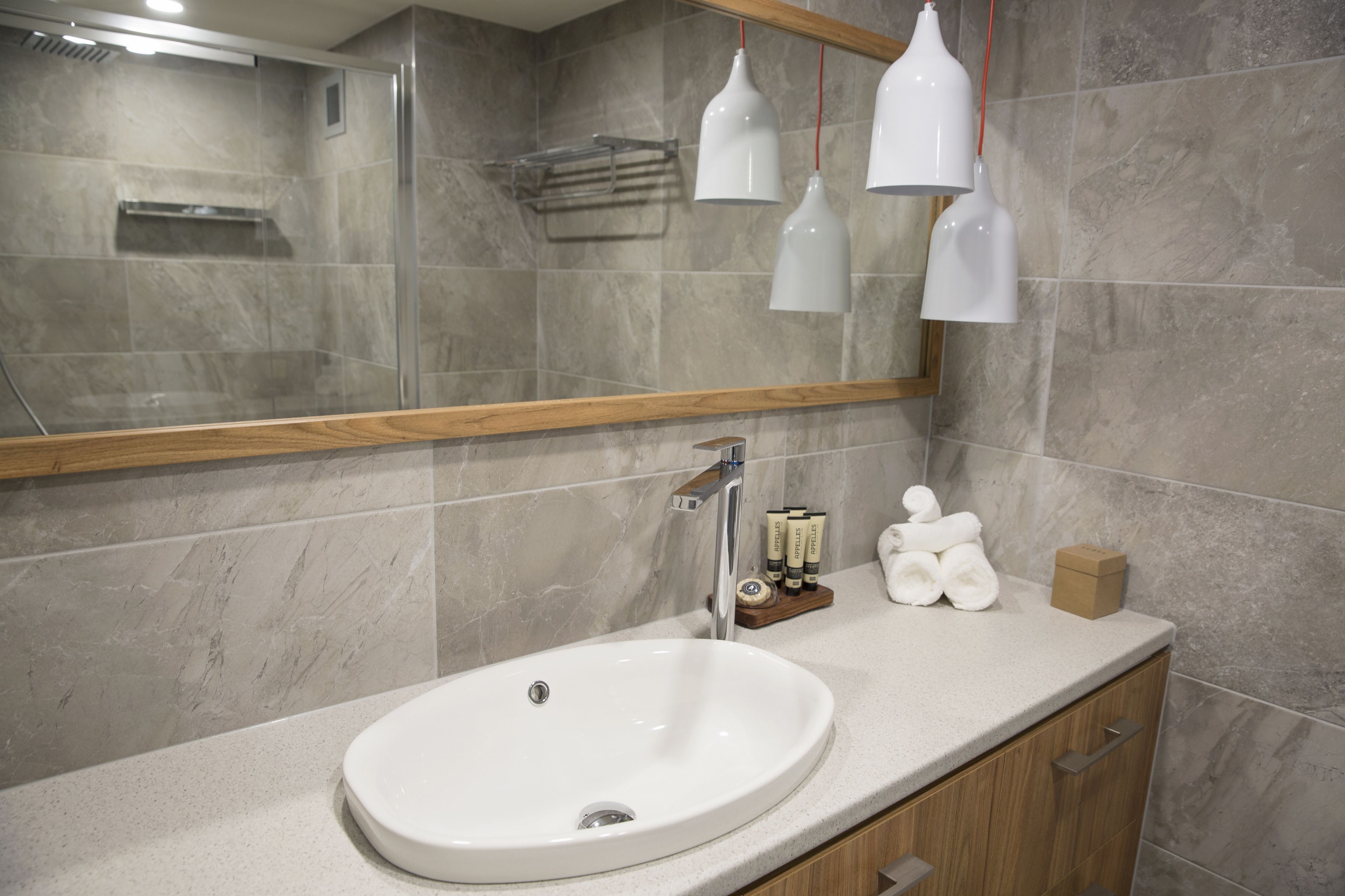 Une salle de bain avec un grand miroir, un lavabo blanc, des meubles en bois et un porte-serviettes.