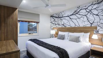 A bedroom with a large bed, a ceiling fan, a window with blinds, and a wall with a tree branch design.