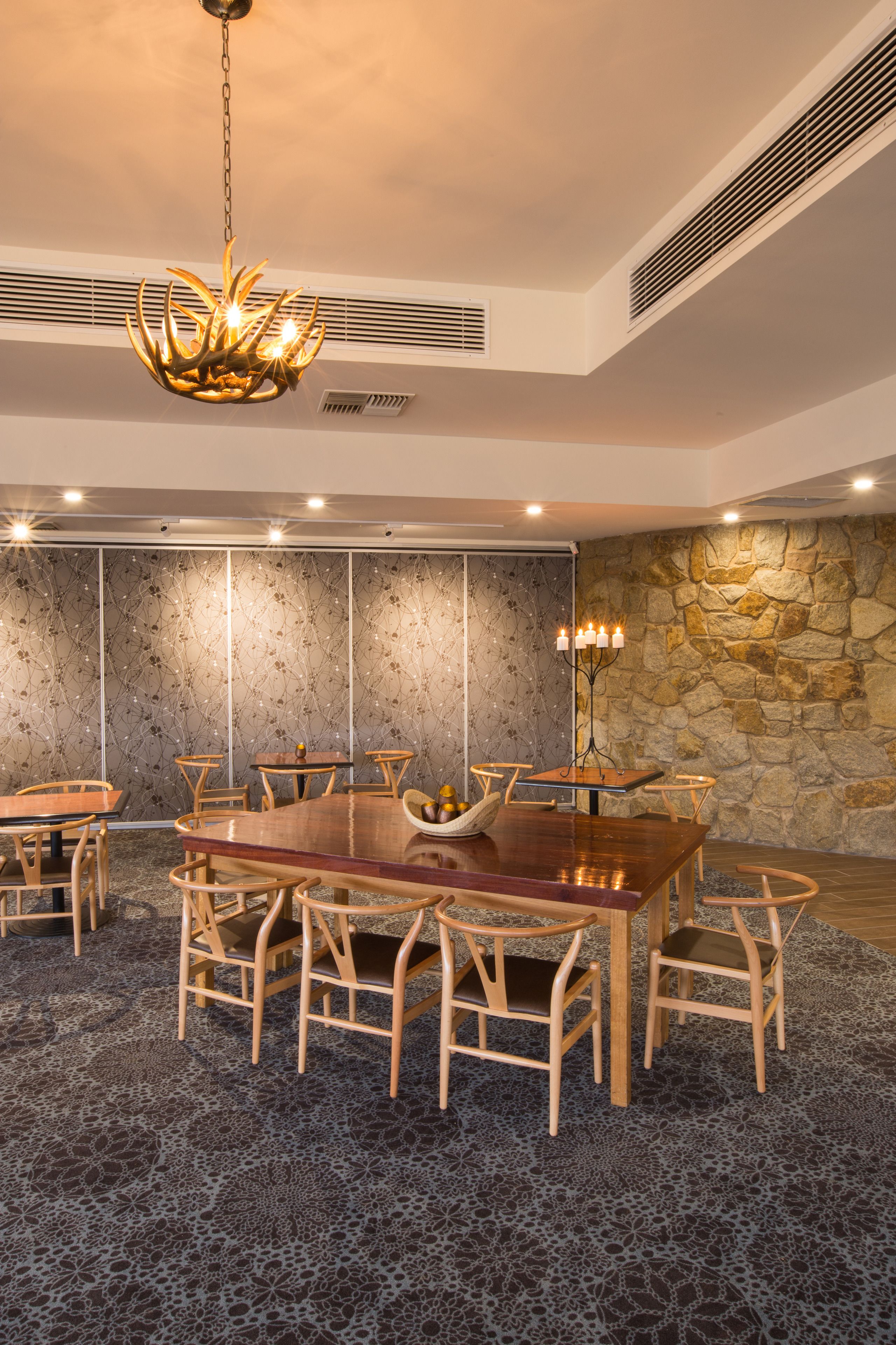 A conference room with a large wooden table, multiple chairs, a decorative chandelier, and a stone wall.