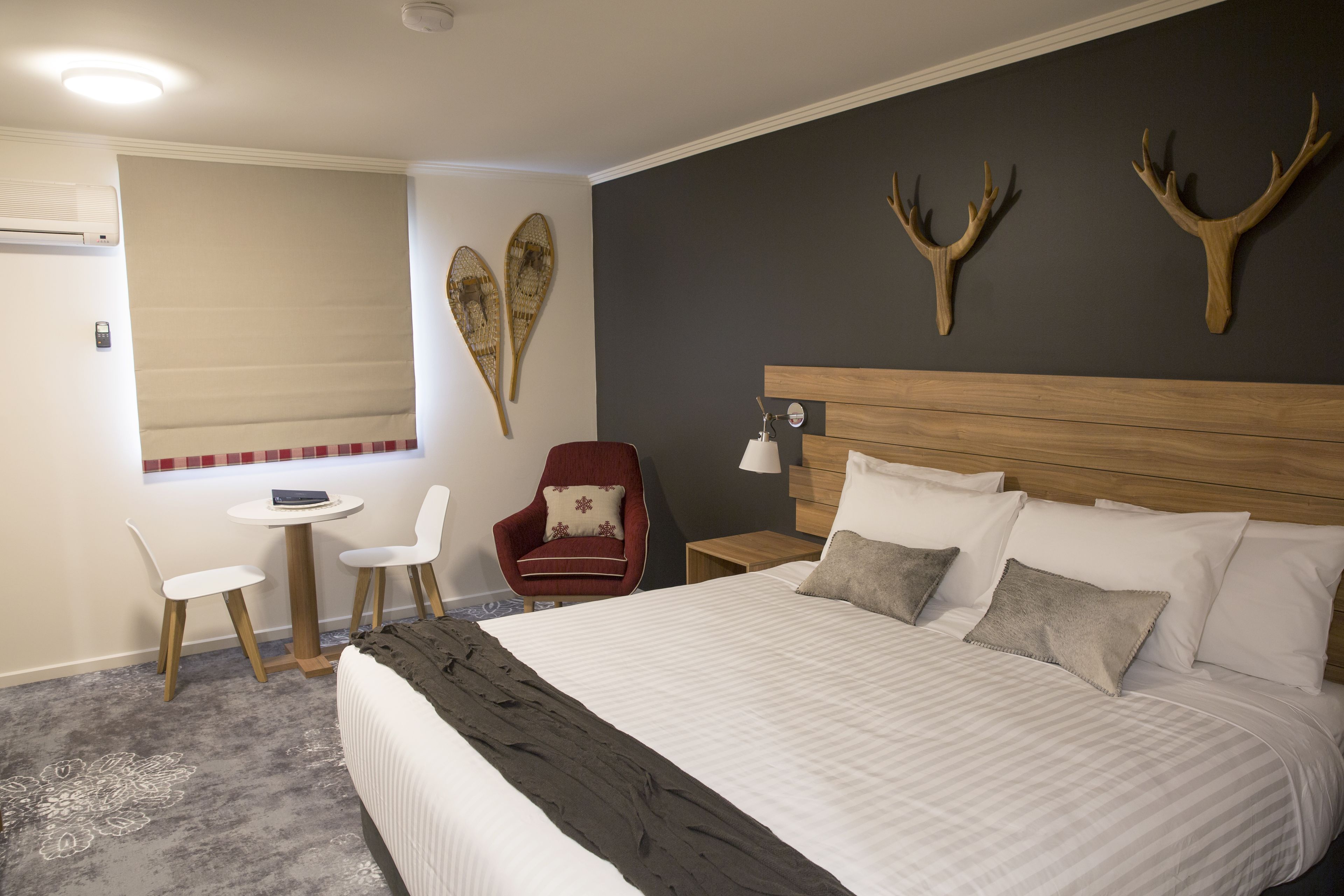 A hotel room with a large bed, a small desk with two chairs, a red armchair, and decorative wall art.