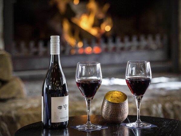 A bottle of wine, two glasses, and a decorative bowl on a table with a fireplace in the background. - The Sebel Pinnacle Valley Resort (Merrijig)
