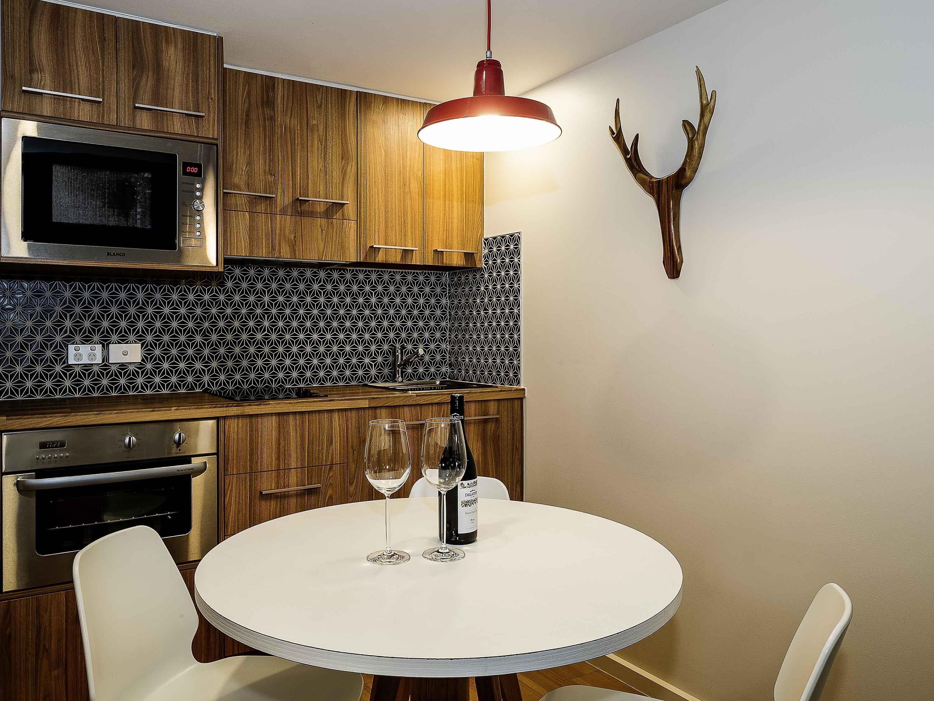 A modern kitchen with wooden cabinets, a microwave, a sink, and a round dining table with two wine glasses and a bottle.