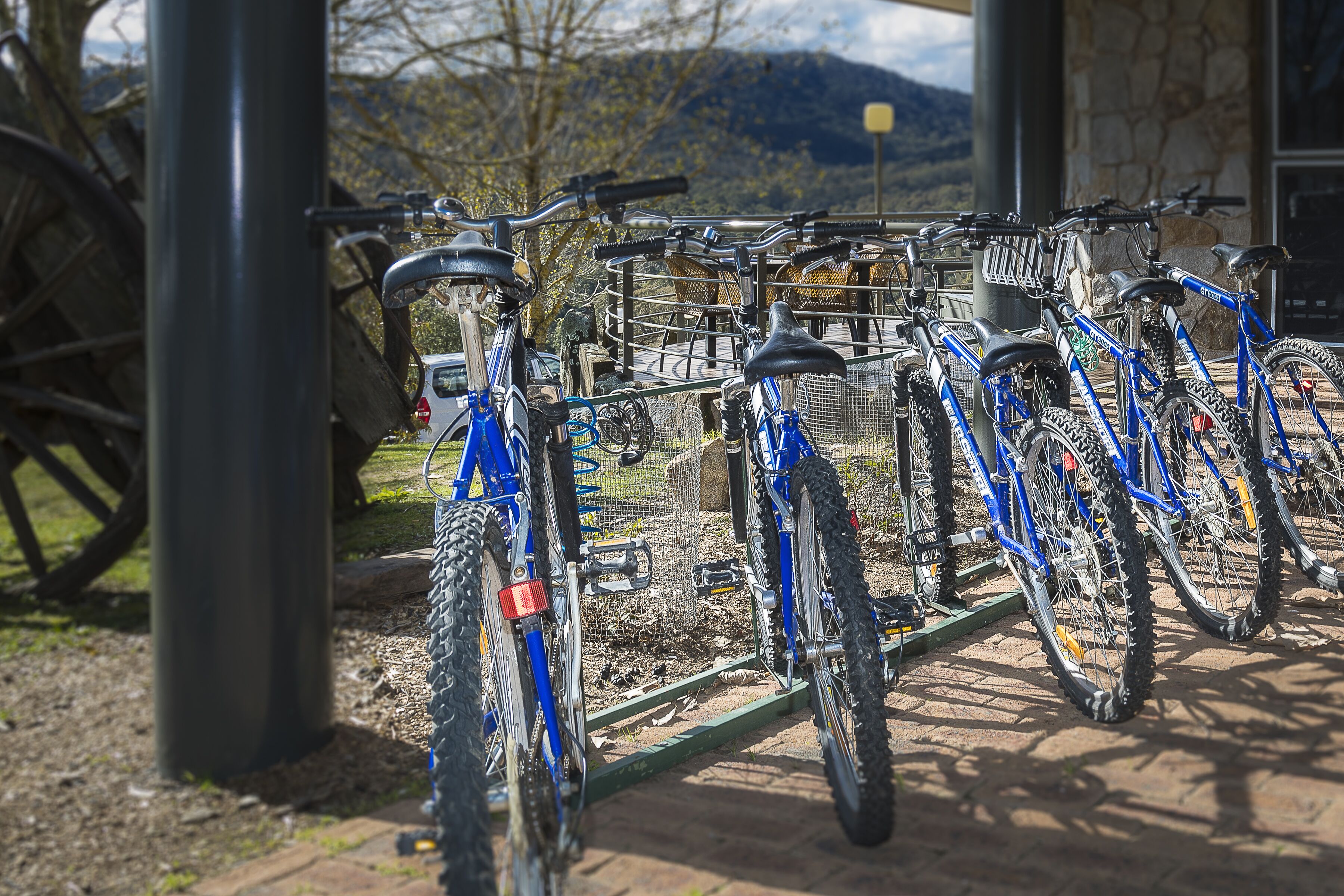 Una fila di biciclette parcheggiate in un’area esterna con un muro di pietra e vista sulle montagne sullo sfondo.