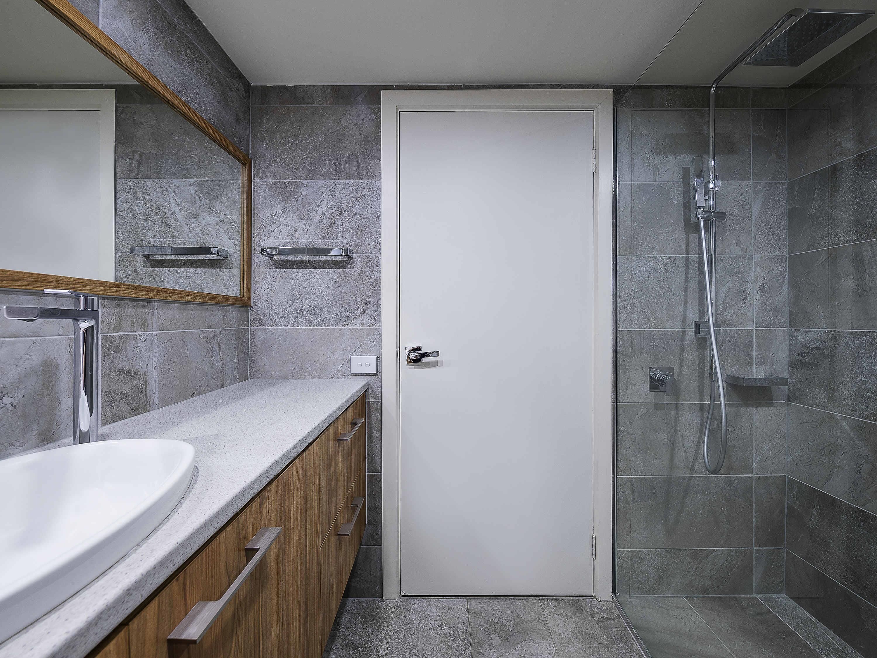 Uma casa de banho moderna com porta branca, lavatório, espelho e zona de duche.