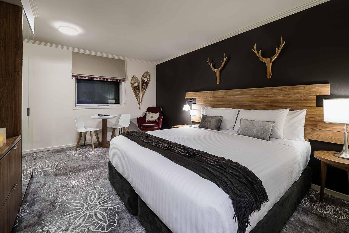 A hotel room with a large bed, a desk with a chair, a TV, and a wall-mounted TV.