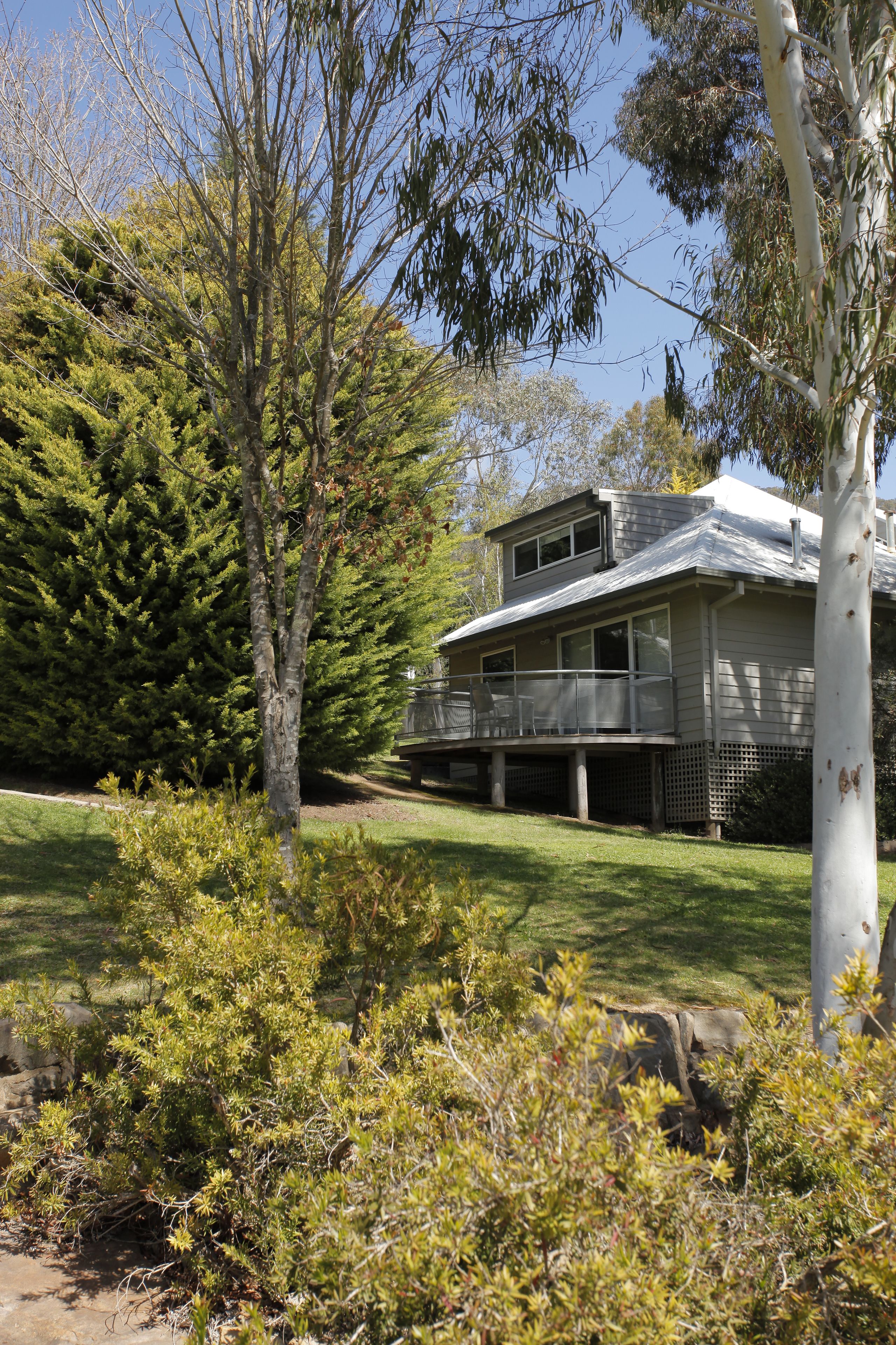 A two-story house with a balcony, surrounded by dense greenery and trees.