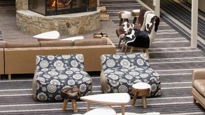 A cozy lounge area with a stone fireplace, patterned seating, and a view of the interior. - The Sebel Pinnacle Valley Resort (Merrijig)